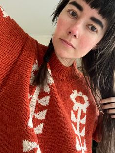 a woman with long black hair is wearing an orange sweater and has her hand on her shoulder