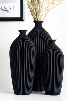 two black vases sitting next to each other on top of a white countertop