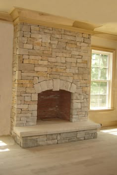 an empty room with a stone fireplace in the center and two windows on either side