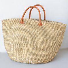 Sisal is a flowering plant that has been cultivated and naturalized in Kenya and the strong fibers that come from it are used to make various items from rope to bags. These durable baskets can handle a heavy load without breaking a sweat while looking handsome at the same time! Woven from natural sisal plant fibers with leather handles. A Kenyan market artisan partnership. Learn more about our artisans' handmade products here. Details: 14" T 20.5" W Colors and designs vary due to the handmade na Natural Bucket Bag With Braided Handles For Market, Natural Crochet Jute Bag With Rolled Handles, Large Natural Straw Bag, Light Brown Bucket Straw Bag With Braided Handles, Natural Basket Crochet Bag For Market, Natural Crochet Basket Bag For Market, Large Natural Eco-friendly Straw Bag, Beige Bucket Straw Bag For Market, Large Natural Straw Bag For Daily Use