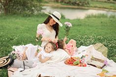 a woman and child sitting on a blanket in the grass