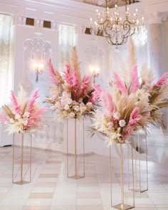 three tall vases with pink and white flowers in front of a chandelier