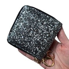 a hand holding a black and silver glittered purse with two gold rings on it