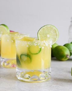 two glasses filled with lemonade and limes on a table next to some limes