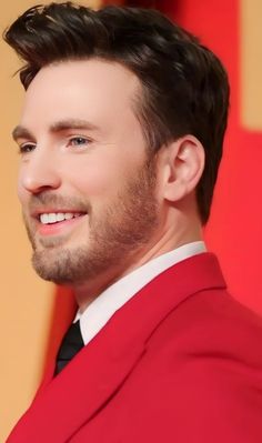 a man in a red suit smiling at the camera with his hair pulled back and wearing a black tie