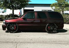 a maroon suv parked in front of a building with black rims and red tires