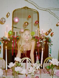 a woman sitting in front of a table with candles and ornaments on top of it