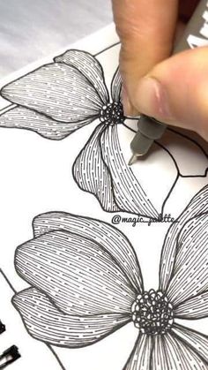 someone is drawing flowers on paper with a pen and inking them into their own designs