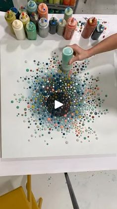 someone is painting on a white table with lots of paint and crayons in the background