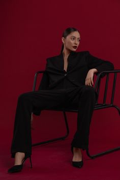 a woman is sitting on a chair with her legs crossed, wearing black pants and heels