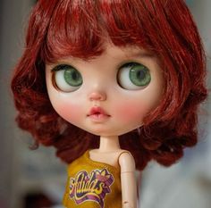 a close up of a doll with red hair and green eyes wearing a yellow shirt