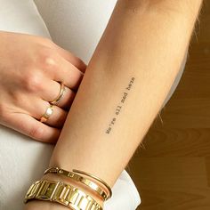 a woman's arm with two gold bracelets on her left wrist and the word love is written in cursive font