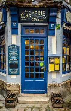 an old building with blue doors and windows on the outside, in front of a cobblestone sidewalk