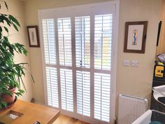 a living room with wooden floors and white shutters on the doors, along with a potted plant