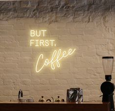 a neon sign that says but first coffee on a brick wall next to a blender