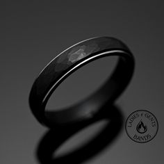 a wedding ring with a black diamond in the center on a gray background and a logo