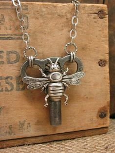 a metal key with a bee on it is sitting on a wooden box and has a chain attached to it