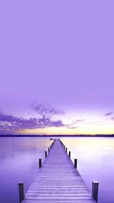 a dock that is sitting in the middle of some water at sunset with purple sky and clouds