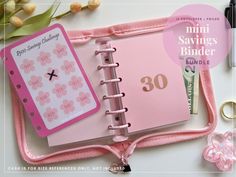 a pink mini savings binder next to some pens and scissors on a white table