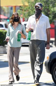 a man and woman walking down the street wearing masks