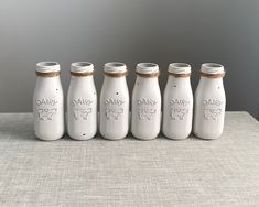 six white glass milk bottles lined up in a row on top of a gray table