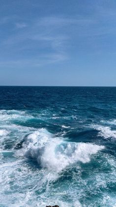 an ocean view with waves crashing on the rocks and blue sky in the back ground