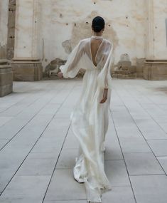 the back of a woman's dress as she walks through an empty room with columns