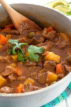 a pot filled with meat and vegetables on top of a table next to a wooden spoon