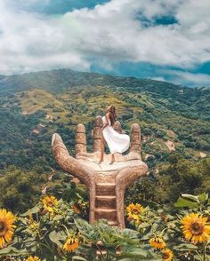 a woman sitting on top of a giant hand statue with sunflowers in the foreground