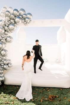 a bride and groom walking through an inflatable arch with silver balls on it