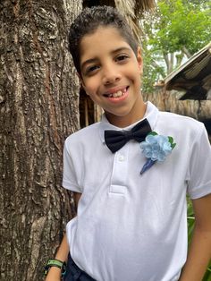 a young boy standing next to a tree wearing a white shirt and blue bow tie