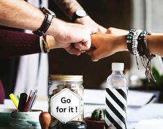 two people shaking hands over a table with bottles and other items on it that says go for it