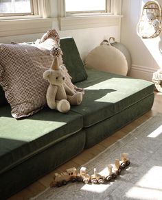 a stuffed animal sitting on top of a green couch in a living room next to pillows