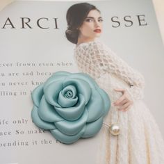 a woman in a white dress holding a blue rose brooch on top of a book