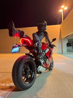 a person riding on the back of a red motorcycle in front of a building at night