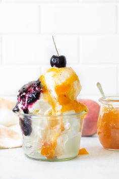 an ice cream sundae in a glass bowl with fruit on top and two jars next to it