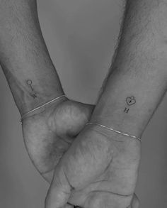 two people holding hands with tattoos on their wrists and one has a heart in the middle