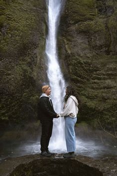 two people standing in front of a waterfall