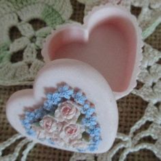 two pink heart shaped soaps with blue flowers on them sitting on a lace doily