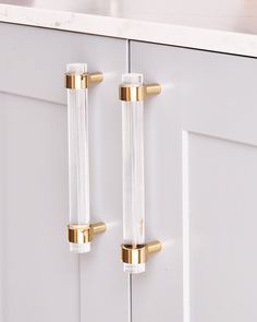 two clear glass door handles on a white cabinet with gold trim and knobs in the middle