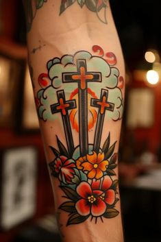 a cross tattoo on the leg with flowers and clouds in the sky behind it,