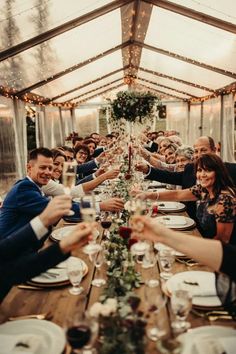 a group of people sitting at a long table toasting with wine glasses in front of them