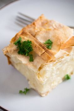 a piece of food on a white plate with a fork in the middle and parsley on top