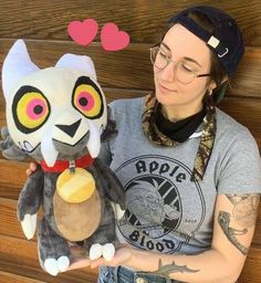 a woman holding a stuffed animal in front of a wooden wall with hearts on it