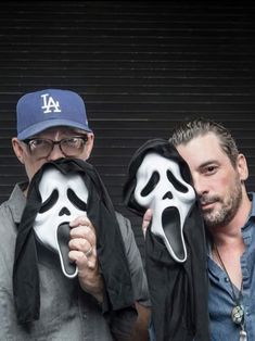 two men are holding up masks with faces painted on them