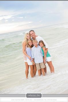 a family standing in the ocean with their arms around each other and posing for a photo