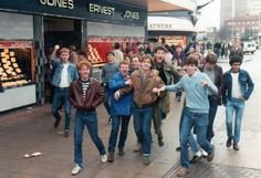 a group of young men walking down a street in front of a store with their arms around each other