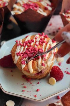 a pastry with white icing and red sprinkles on it sitting on a plate next to raspberries