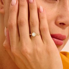 a woman holding her hand up to her face while wearing a gold ring with a flower on it