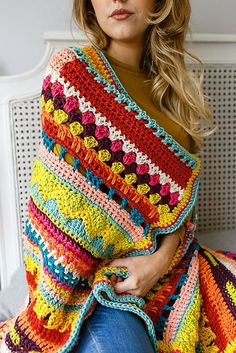 a woman sitting on a bed wearing a colorful crocheted blanket